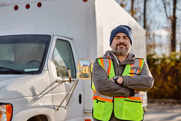 Smiling truck driver with arms crossed on parking lot looking at camera.