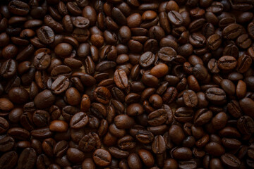 Coffee grains form the background. View from above. Intense brown color of roasted coffee beans. A large number of coffee beans are on the table. Invigorating background.