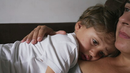 Pensive small boy leaning on mother chest about to nap. Child lost in thought lying on mom body