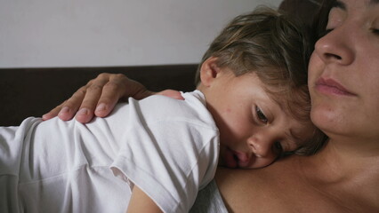 Pensive small boy leaning on mother chest about to nap. Child lost in thought lying on mom body
