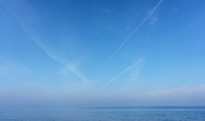 Jet plane contrails over clear blue sky and sea.