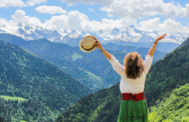 Elegant woman at the mountains. Happy girl with wavy hair. Freedom concept. The background of the majestic mountains of the Caucasus and wooden fence. Svaneti, Georgia.
