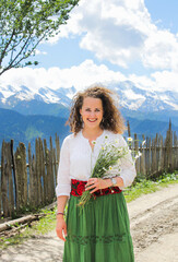 Elegant woman in the mountains. Happy girl with wavy hair holding a bouquet of daisies. The background of the majestic mountains of the Caucasus. Svaneti, Georgia.