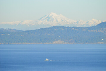 A tugboat traverses and ocean pathway with the San Juan Islands and the beautiful Mount Baker in behind