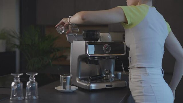 Caucasian female is filling water tank of espresso machine with fresh water