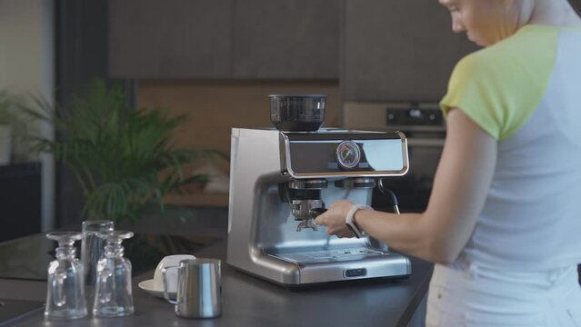 Caucasian female is inserting portafilter into the coffee powder outlet .