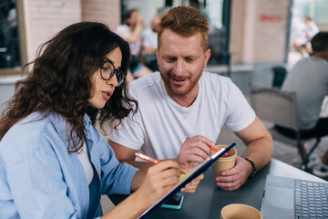 Caucasian male and female colleagues analyzing and discussing paperwork during business meeting in street cafeteria, intelligent journalists planning organization while cooperate togetherness