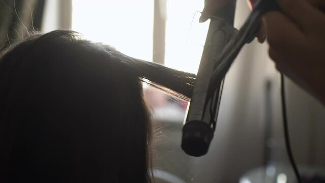 Hairdresser makes the girl's hair with a electric curling iron. Unrecognizable caucasian woman curls her hair, styling. Preparing for the holiday.