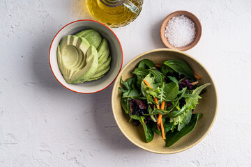 Obraz premium Salad ingredients leaf vegetables and sliced avocado in bowls on white background