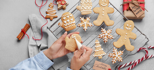 Woman decorating Christmas gingerbread cookies on light background, top view