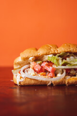 Close-up of a chicken sandwich with lots of vegetables on top of a wooden table.