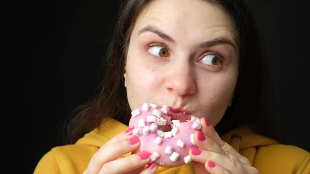 A female glutton eats a donut, bites it many times and looks around. Gluttony, excess weight, weight loss