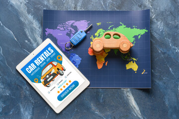 Tablet computer with open page of car rental website, map, key and toy car on blue background