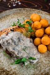 Fried chicken thigh with mushroom sauce and croquettes, fried mashed potato balls with tomatoes and greens, closeup.