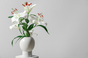 Vase with beautiful lilies on stand near grey wall