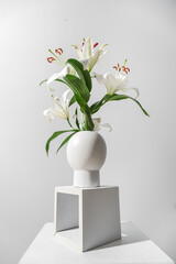 Vase with beautiful lilies on stand near grey wall