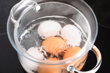 Glass cooking pot with boiling eggs on stove in kitchen, closeup