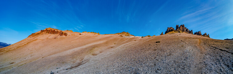 Fototapeta premium Panoramic over a hiking trail at Icelandic landscape of colorful volcanic caldera Askja, in the middle of volcanic desert in Highlands, with red, turquoise volcano soil and blue sky, Iceland.