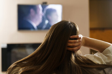 Naklejka premium The girl watches TV, sits in the living room at home in the evening.