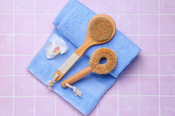 Massage brushes, towel and flower on color tile background
