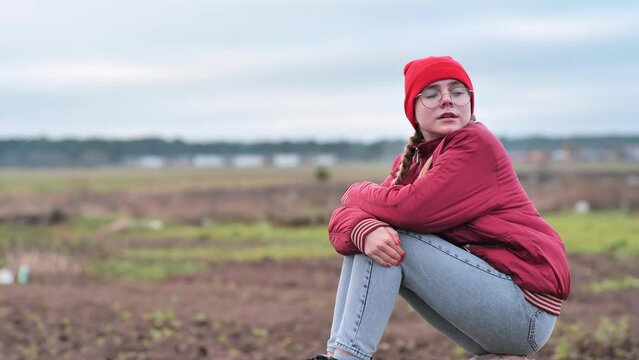 A sad teenage girl sits on a rock in a field and cries.