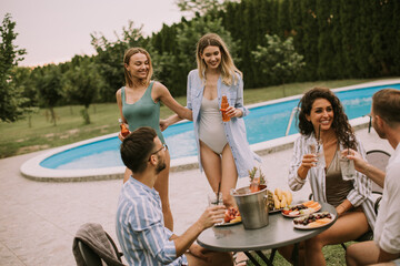 Group of young people cheering with cider by the pool in the garden