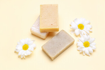 Soap bars and chamomile flowers on color background