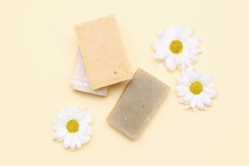Soap bars and chamomile flowers on color background