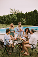 Group of young people cheering with cider by the pool in the garden