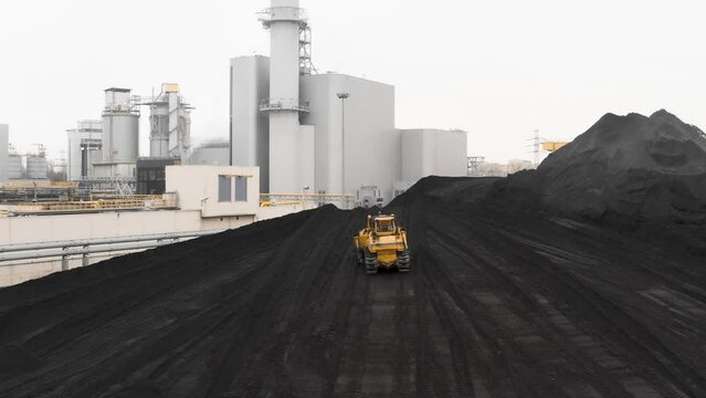 A crawler bulldozer rakes coal reserves into a large pile for heating housing during the heating season in a fossil fuel warehouse of a thermal power plant.