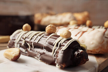 Board with delicious eclairs on wooden table, closeup