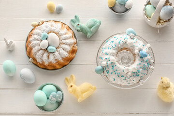 Composition with tasty Easter cakes, painted eggs and bunnies on white wooden background
