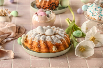 Plate with tasty Easter cake, painted eggs and beautiful tulip flowers on pink tile table