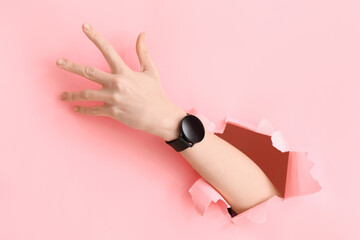 Female hand and smartwatch visible through torn pink paper