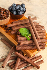 Board with delicious chocolate wafer rolls, blueberries and coffee beans on beige background
