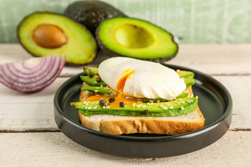 Plate with delicious avocado toast and poached egg on white wooden background