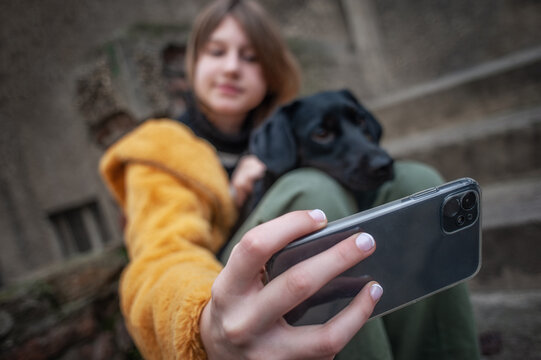 Influencer, teenage girl with a black dog taking a selfie with her smartphone, outdoors in the city streets
