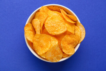 Bowl with delicious potato chips on blue background