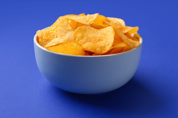 Bowl with delicious potato chips on blue background