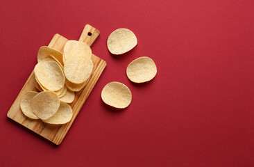 Board with delicious potato chips on red background