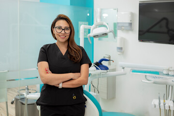 Fototapeta premium Female dentist with arms crossed looking at camera, standing in her medical office