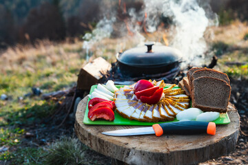 Food is prepared in a cauldron at the campsite. Fat and black bread with vegetables on a wooden table.
