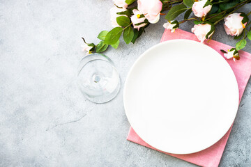 Faestive Table setting with white plate and rose flowers. Table decor for an anniversary or wedding. Flat lay with copy space.