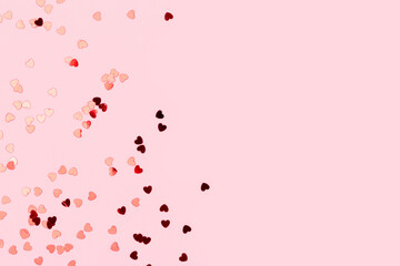 Metallic red confetti in a heart shape scattered on a pink background. Composition with place for...