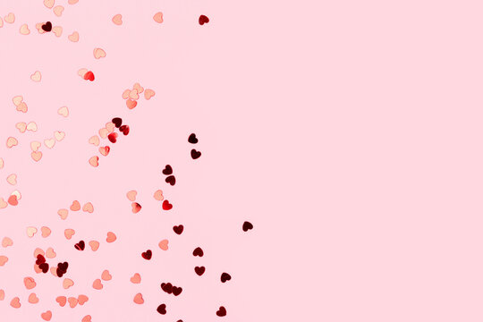 Metallic red confetti in a heart shape scattered on a pink background. Composition with place for text.