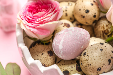 Basket with Easter quail eggs and rose flower on pink background, closeup