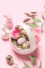 Basket with Easter quail eggs, rose flowers, eucalyptus branches and bunnies on pink background