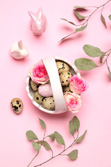 Basket with Easter quail eggs, rose flowers, eucalyptus branches and bunnies on pink background