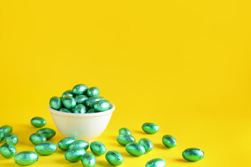 Bowl of chocolate Easter eggs in color foil on yellow background