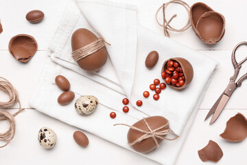 Composition with candies and chocolate Easter eggs tied with thread on white wooden background